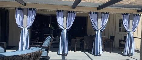 A covered outdoor seating area with wicker furniture and curtains.