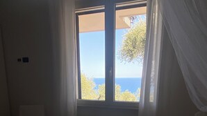 A bedroom with a large window, a radiator, a chair, and a bedside table. - Diano Marino / Rollo 100sqm 4 pers. quiet with sea view (Andora)
