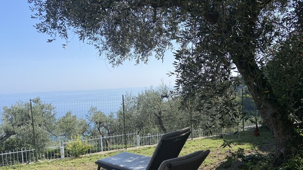 A pair of lounge chairs with cushions, positioned under a tree, overlooking a fenced garden and a view of the sea. - Diano Marino / Rollo 100sqm 4 pers. quiet with sea view (Andora)