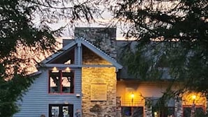 A two-story lodge with a stone facade and a wooden deck. - Cannon Hill Inn (Rowlesburg)