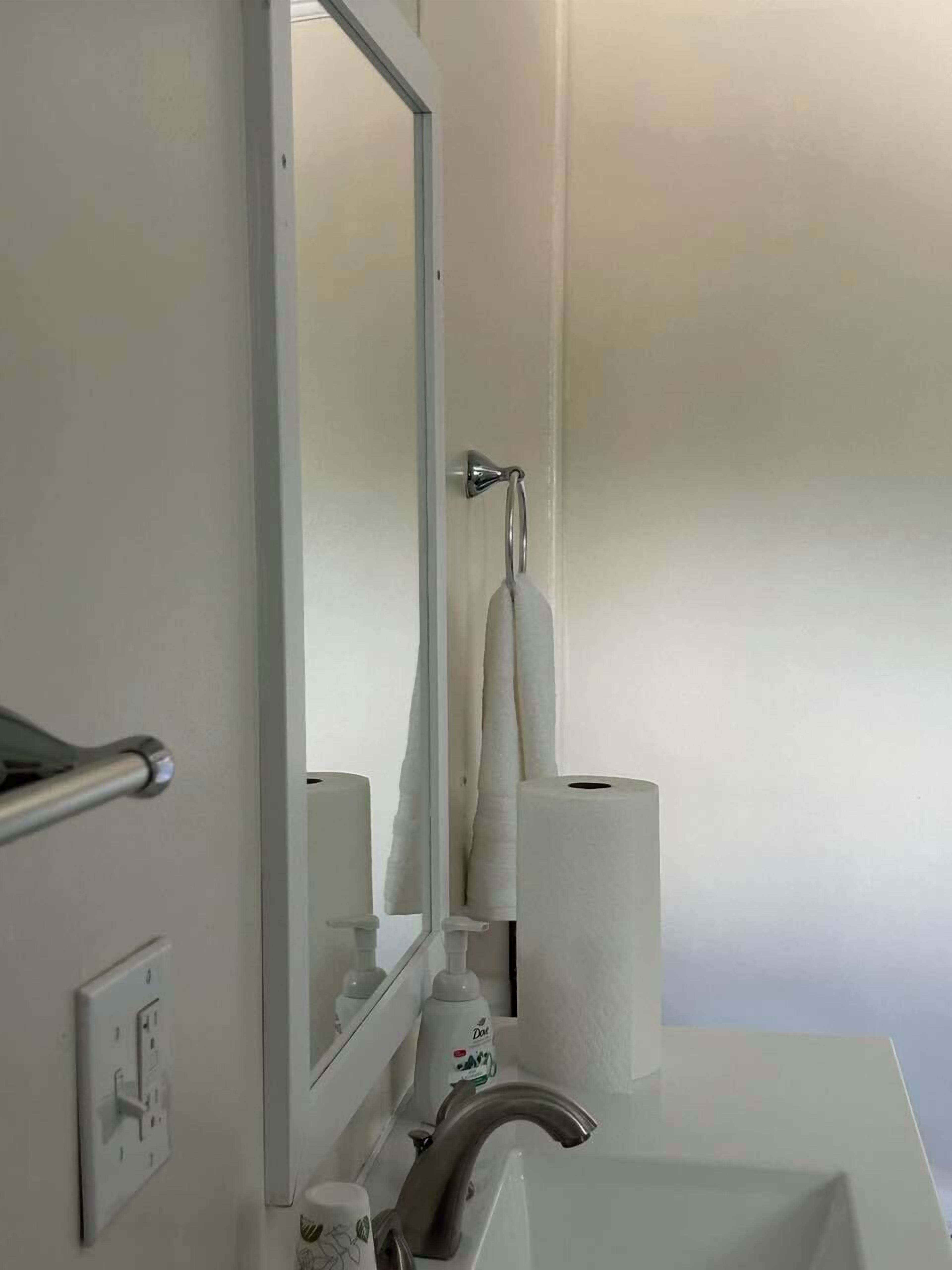 A bathroom with a white sink, a mirror, a towel hanging on the wall, and two rolls of toilet paper.