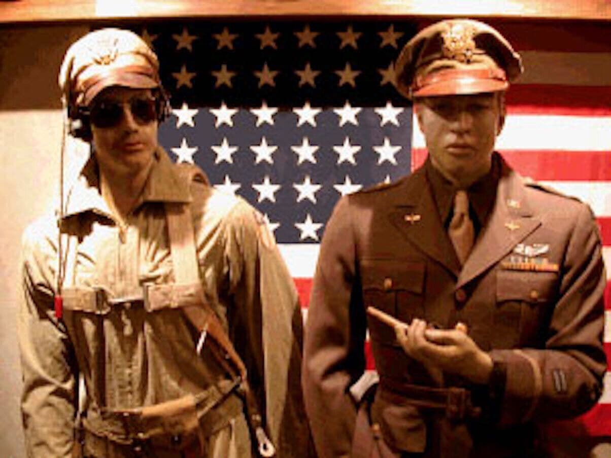Two mannequins dressed in military uniforms with an American flag in the background.