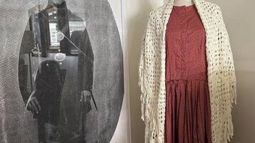 A mannequin dressed in a red dress with a white crochet shawl, standing next to a framed black and white photograph.