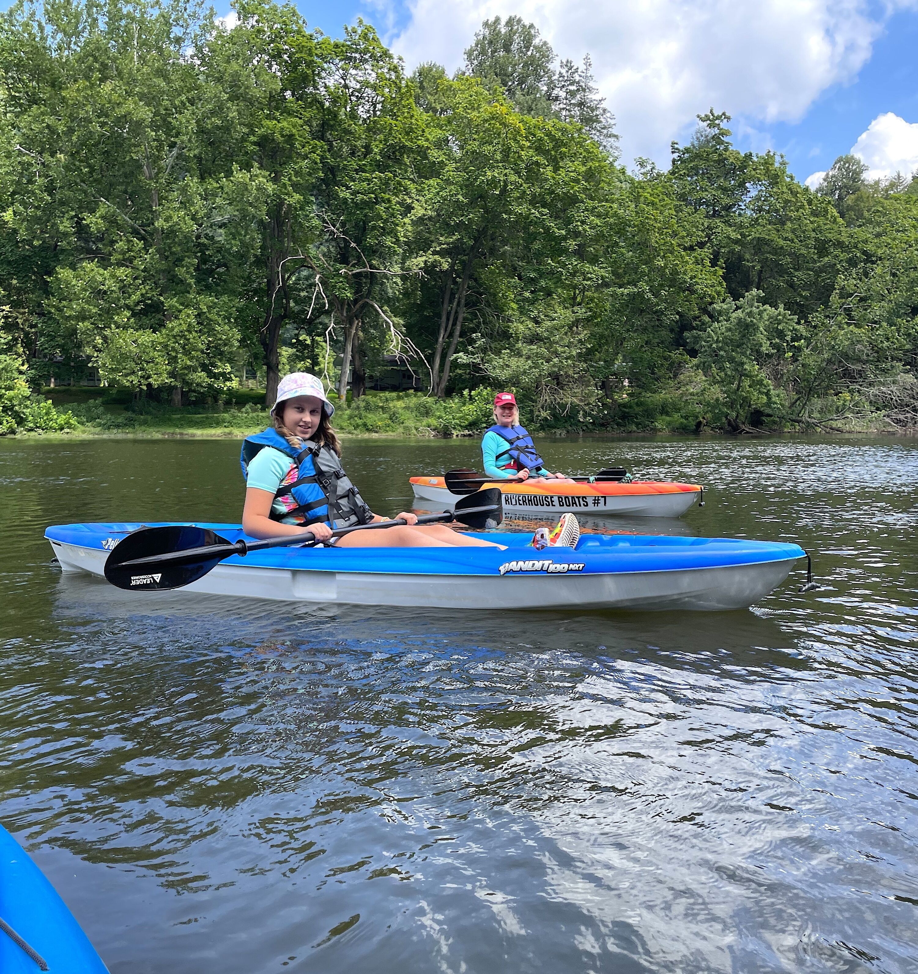 Dos personas remando en kayak por un río tranquilo rodeado de abundante vegetación.