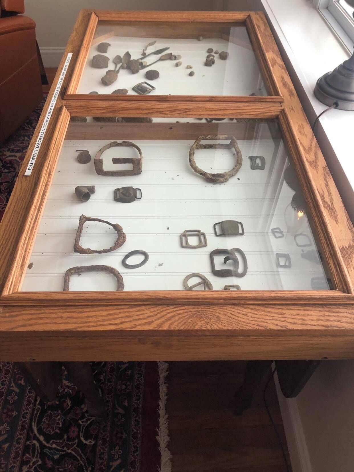 Una vitrina exhibe diversos objetos de metal, como anillos y hebillas, sobre un fondo blanco.