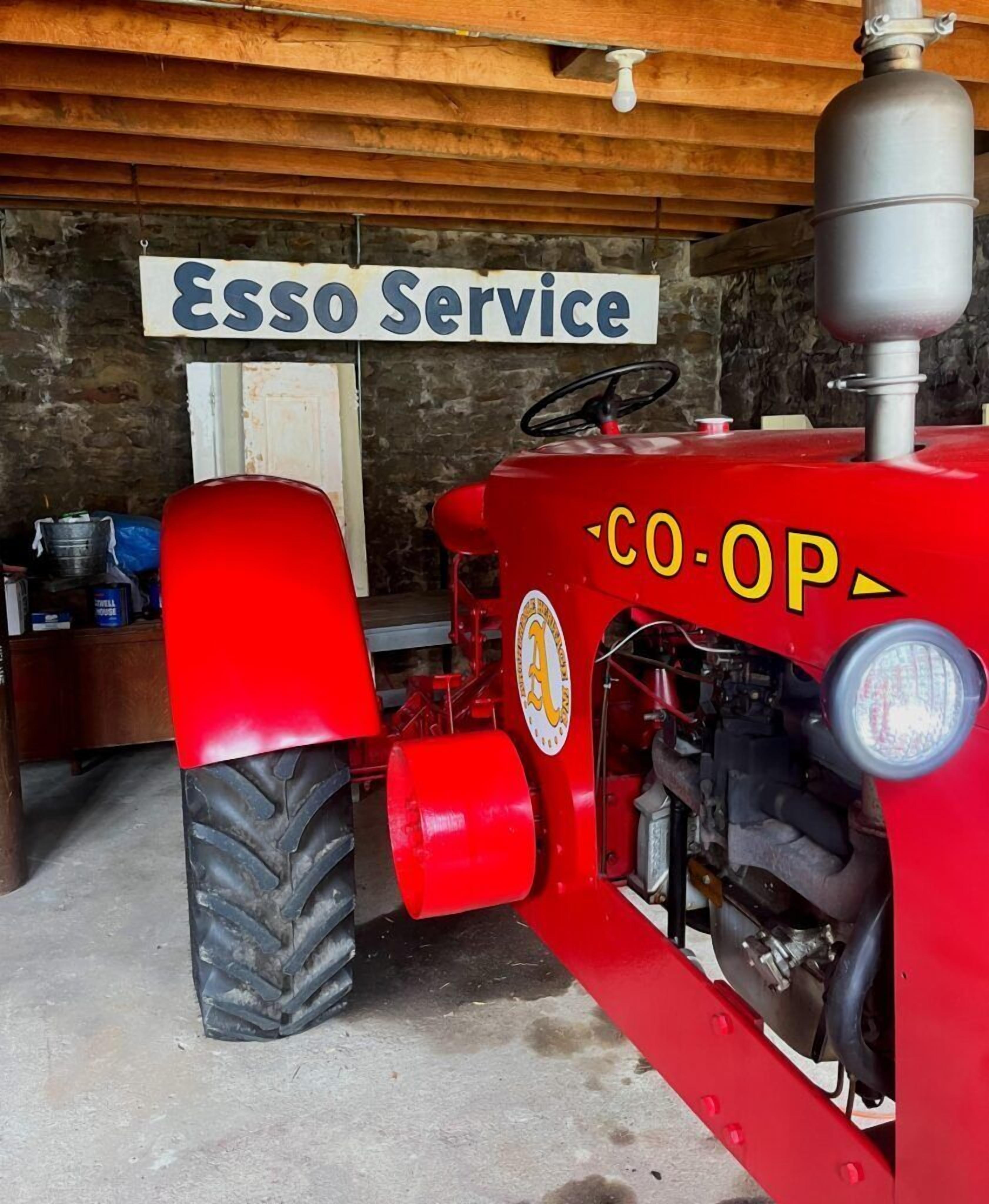Un tractor rojo con un letrero que dice 'Esso Service' en un taller mecánico.