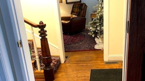 A wooden-floored hallway leading to a living room with a brown leather chair, a small Christmas tree, and a framed picture on the wall. - Cannon Hill Inn (Rowlesburg)