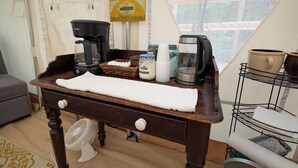 Una stanza accogliente con un tavolo di legno apparecchiato con accessori per preparare il caffè, un asciugamano bianco e un cartello con su scritto “RISE AND SHINE”.