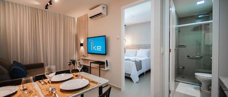 Una habitación de hotel con zona de comedor, televisor, cama y ducha.