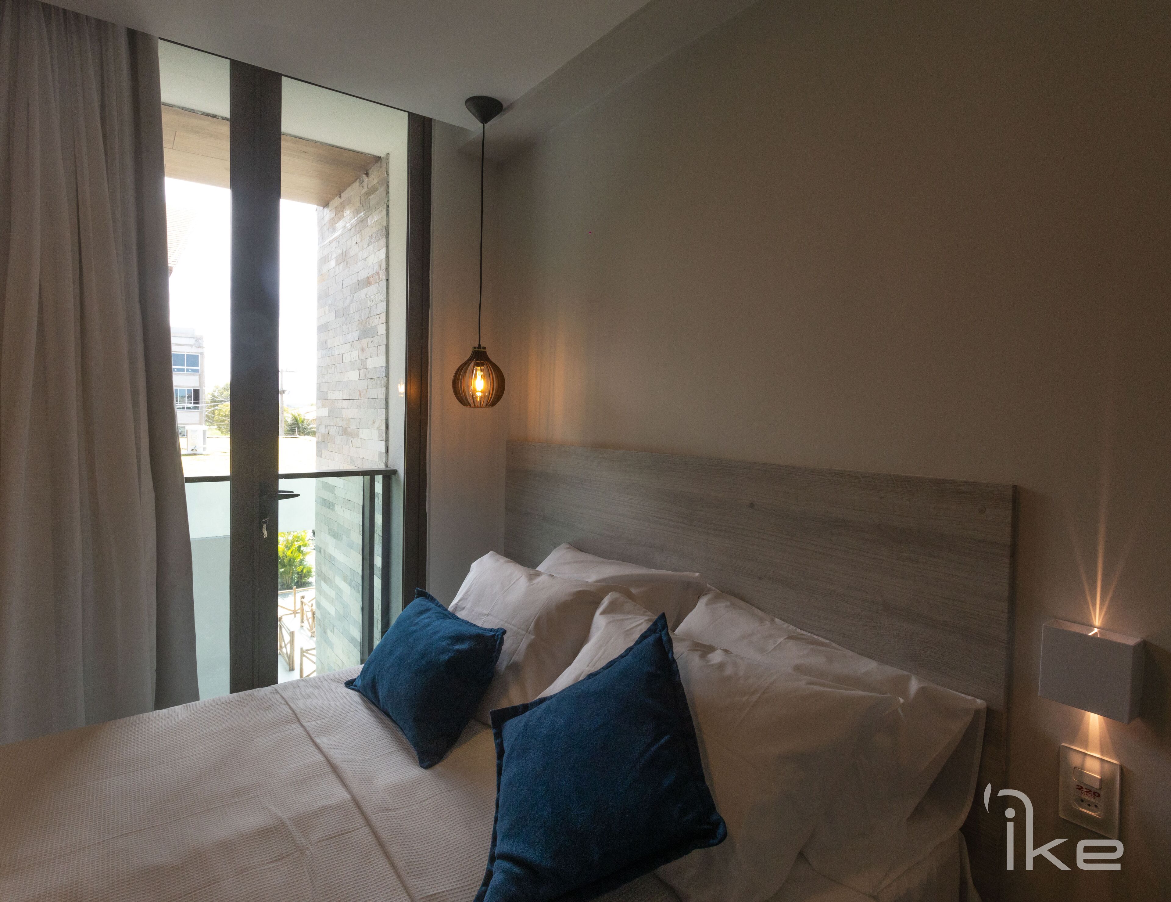 Een moderne hotelkamer met een groot bed, twee kussens, een hanglamp en uitzicht op het landschap door een raam.