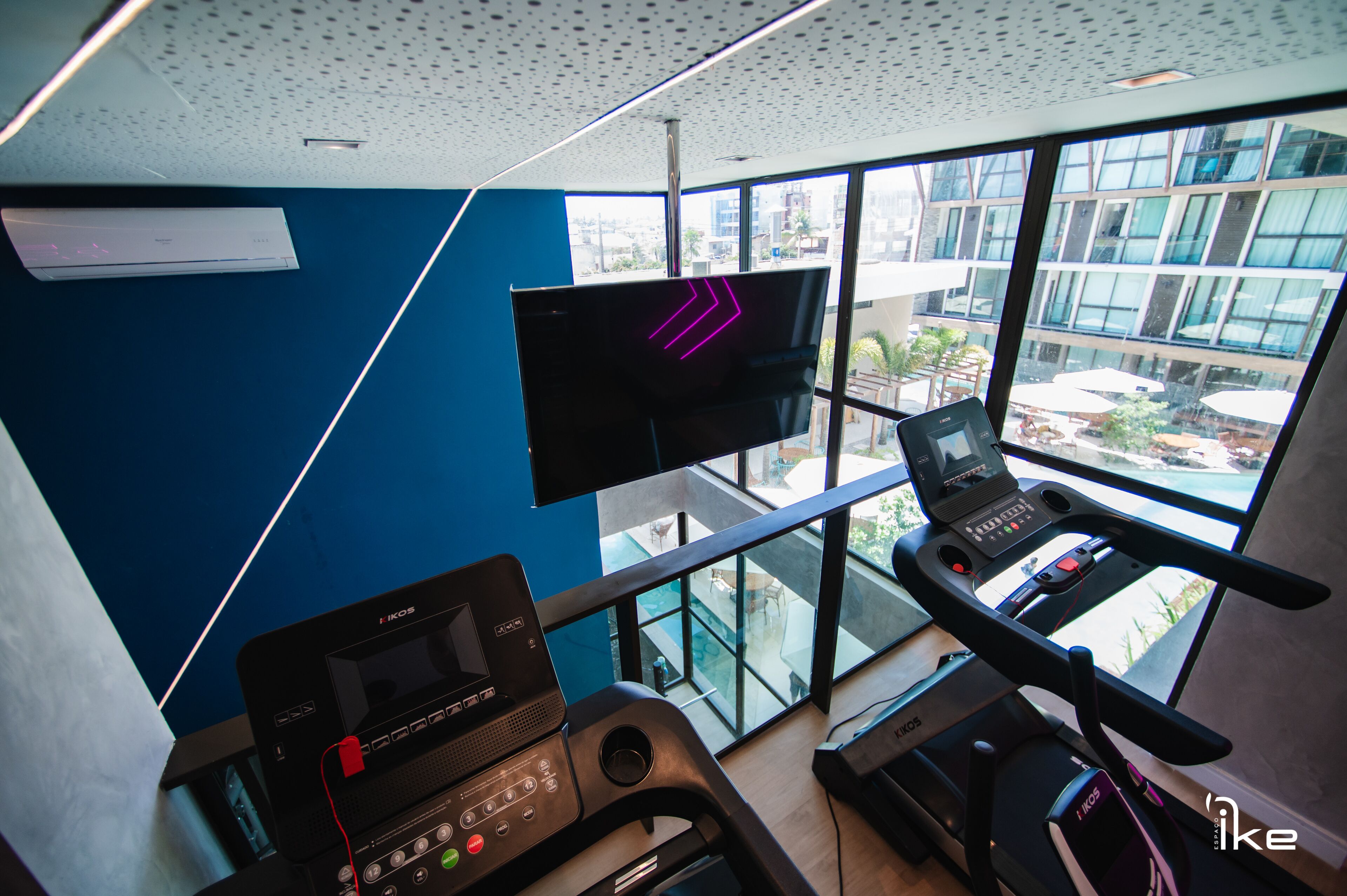 A modern fitness room with a treadmill, a stationary bike, and a TV mounted on the wall.