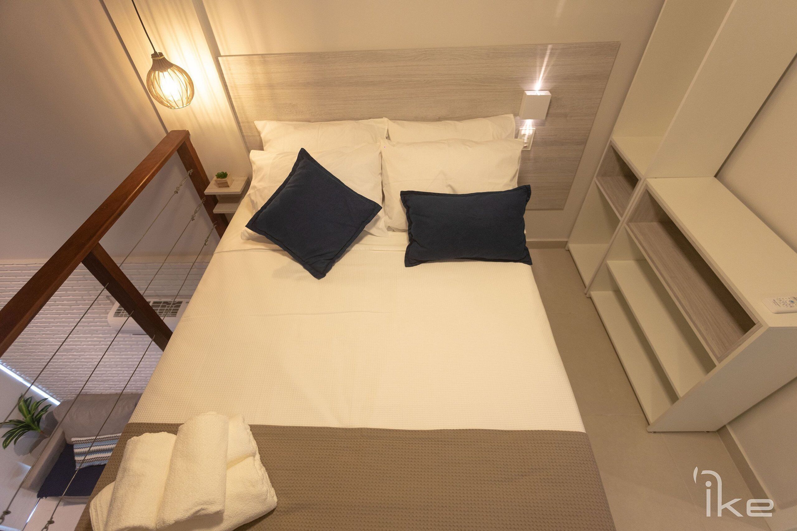 Ein Hotelzimmer mit Bett, Kissen, Nachttisch, Lampe und Blick ins Freie.