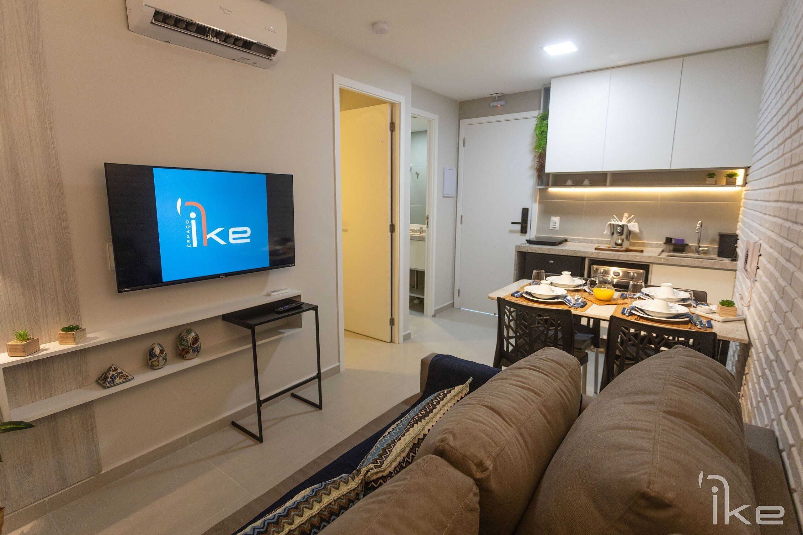 A modern living room with a flat-screen TV, a sofa, a coffee table, and a kitchen area with a dining table.