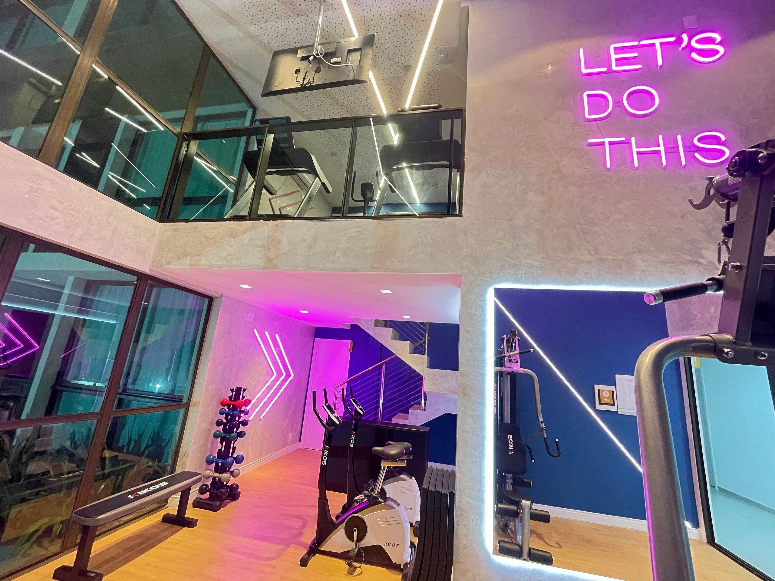 Ett modernt gym med träningsutrustning, en trappa och en neonskylt med texten ”Låt oss köra!”.