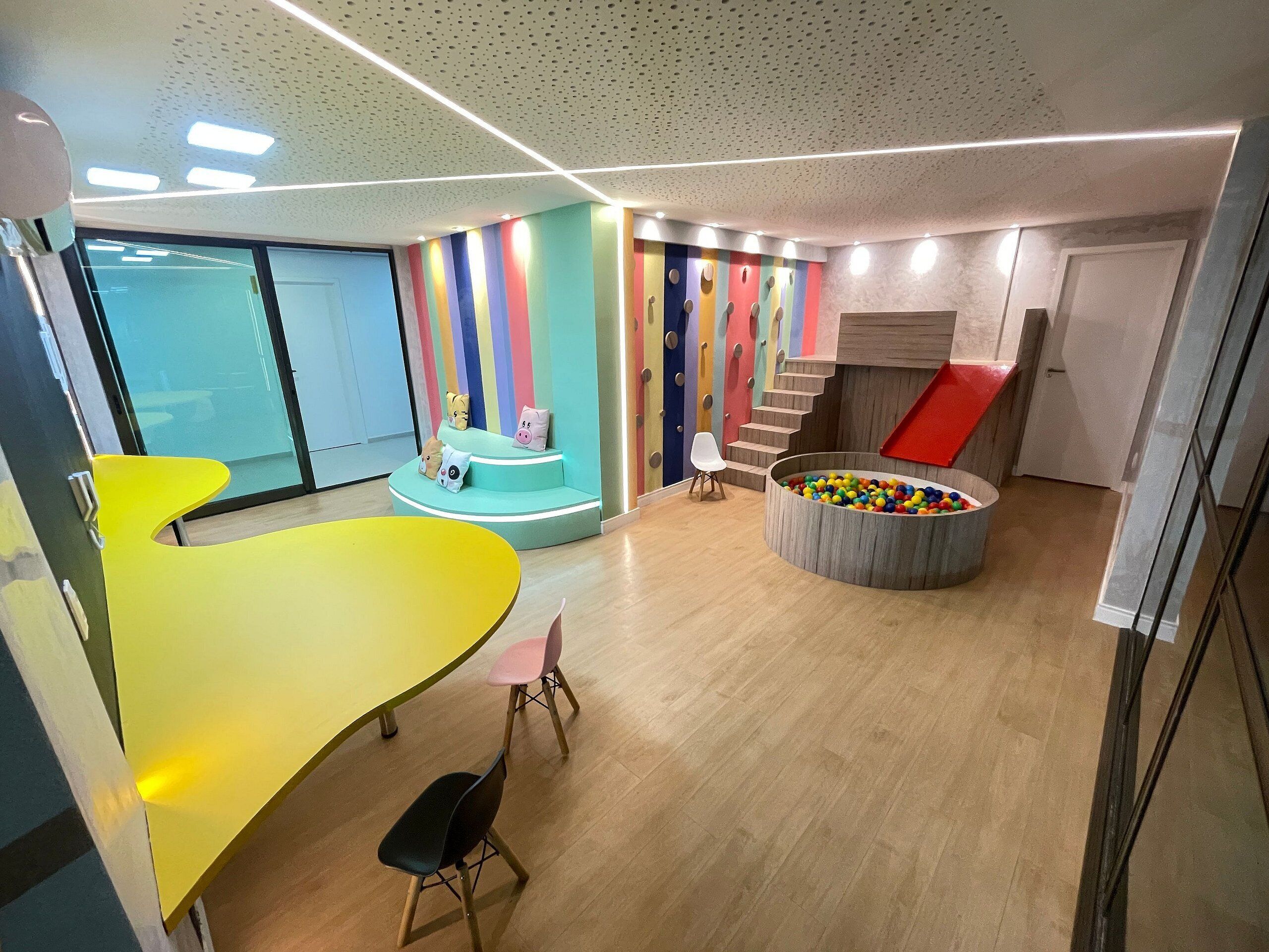 Un interior moderno con una zona de juegos colorida, una mesa amarilla y una escalera.