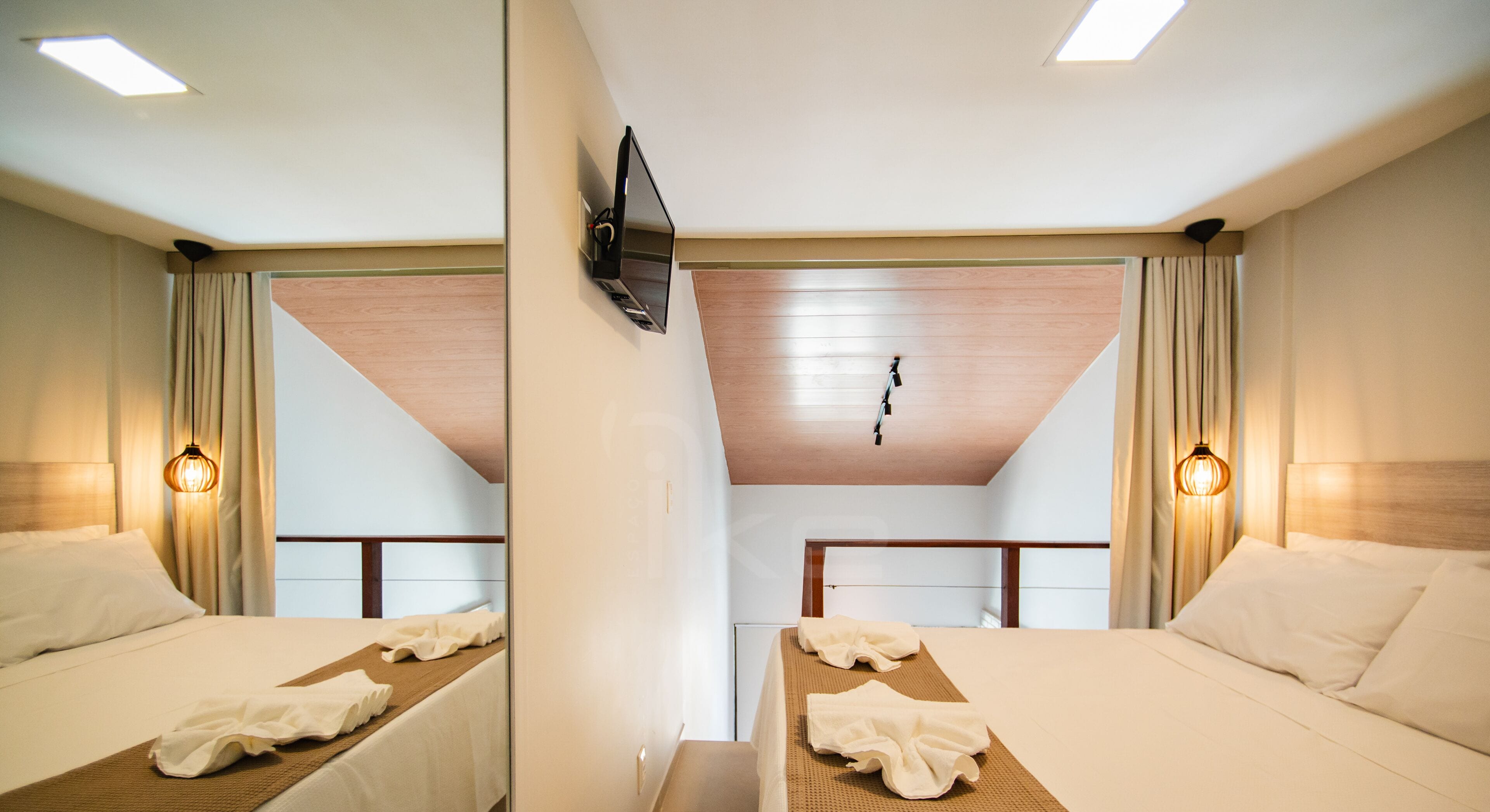 Una habitación de hotel con dos camas, un televisor montado en la pared y una lámpara en el techo.