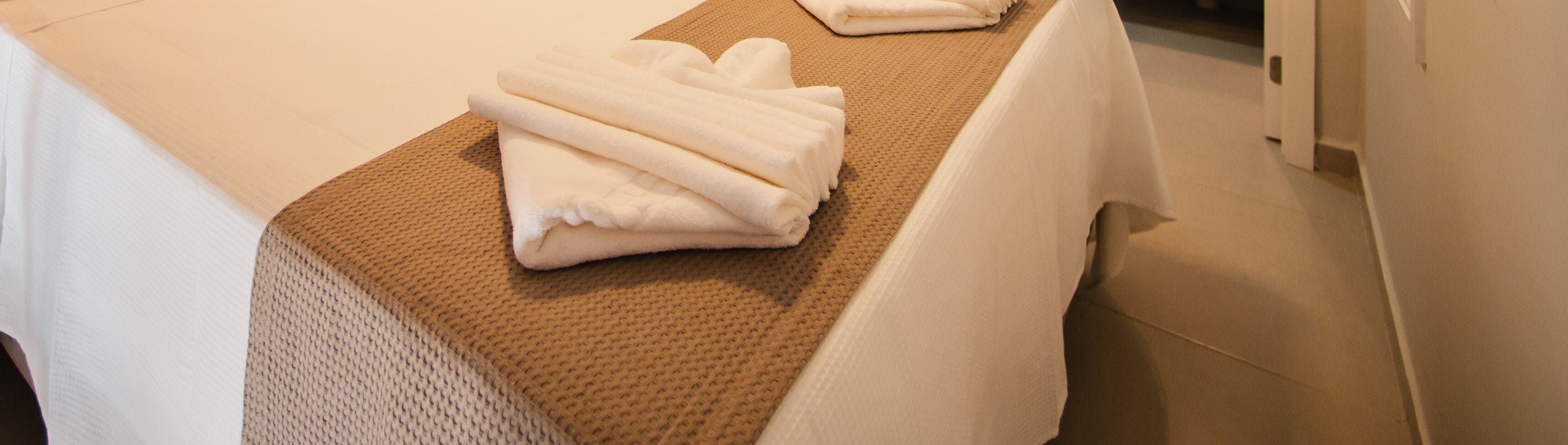 Una toalla blanca doblada con cuidado sobre una alfombra marrón texturizada, probablemente en una habitación de hotel.
