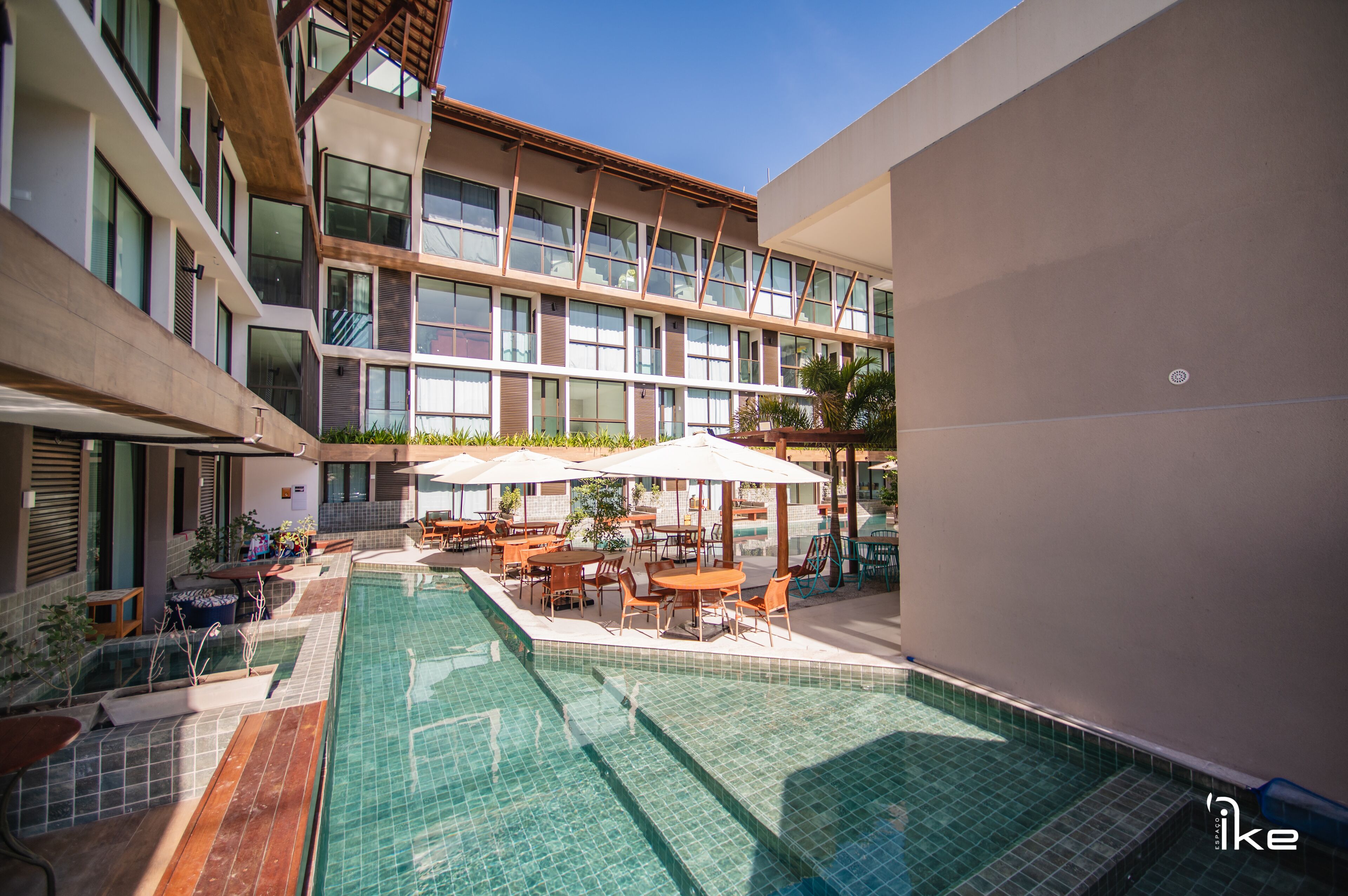 Un hotel moderno con piscina, asientos exteriores y un edificio de varios pisos con grandes ventanales.