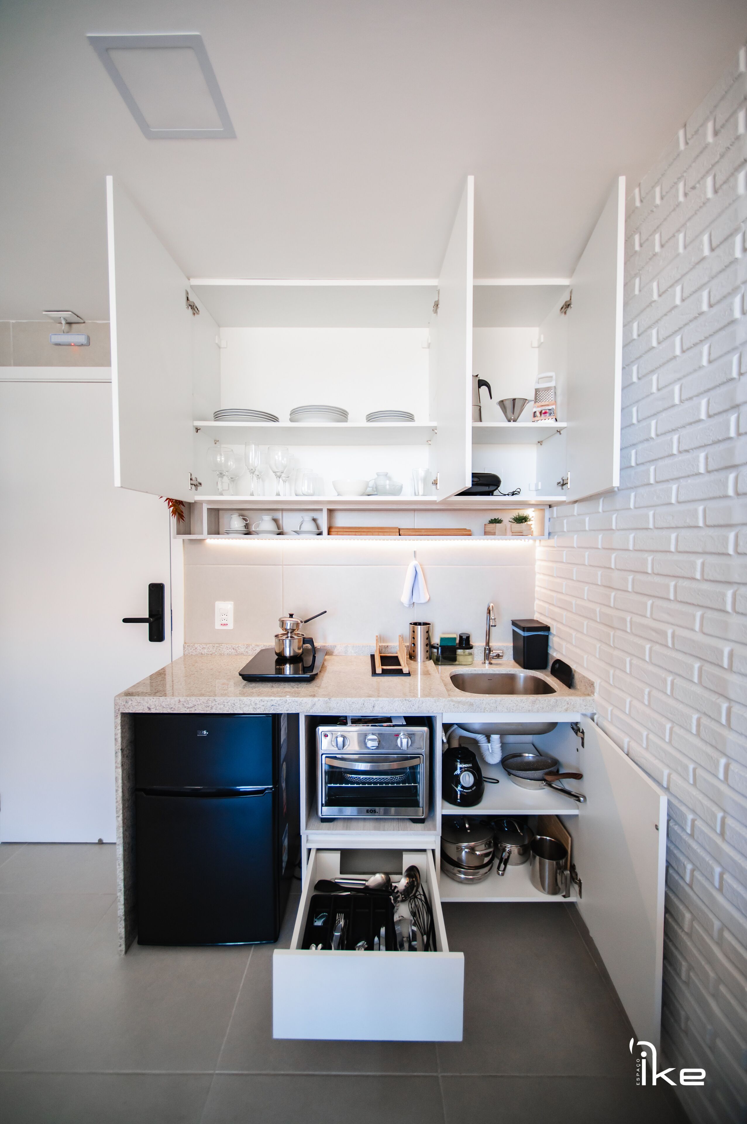 A compact kitchen with built-in appliances, open shelving, and a hidden drawer for utensils.