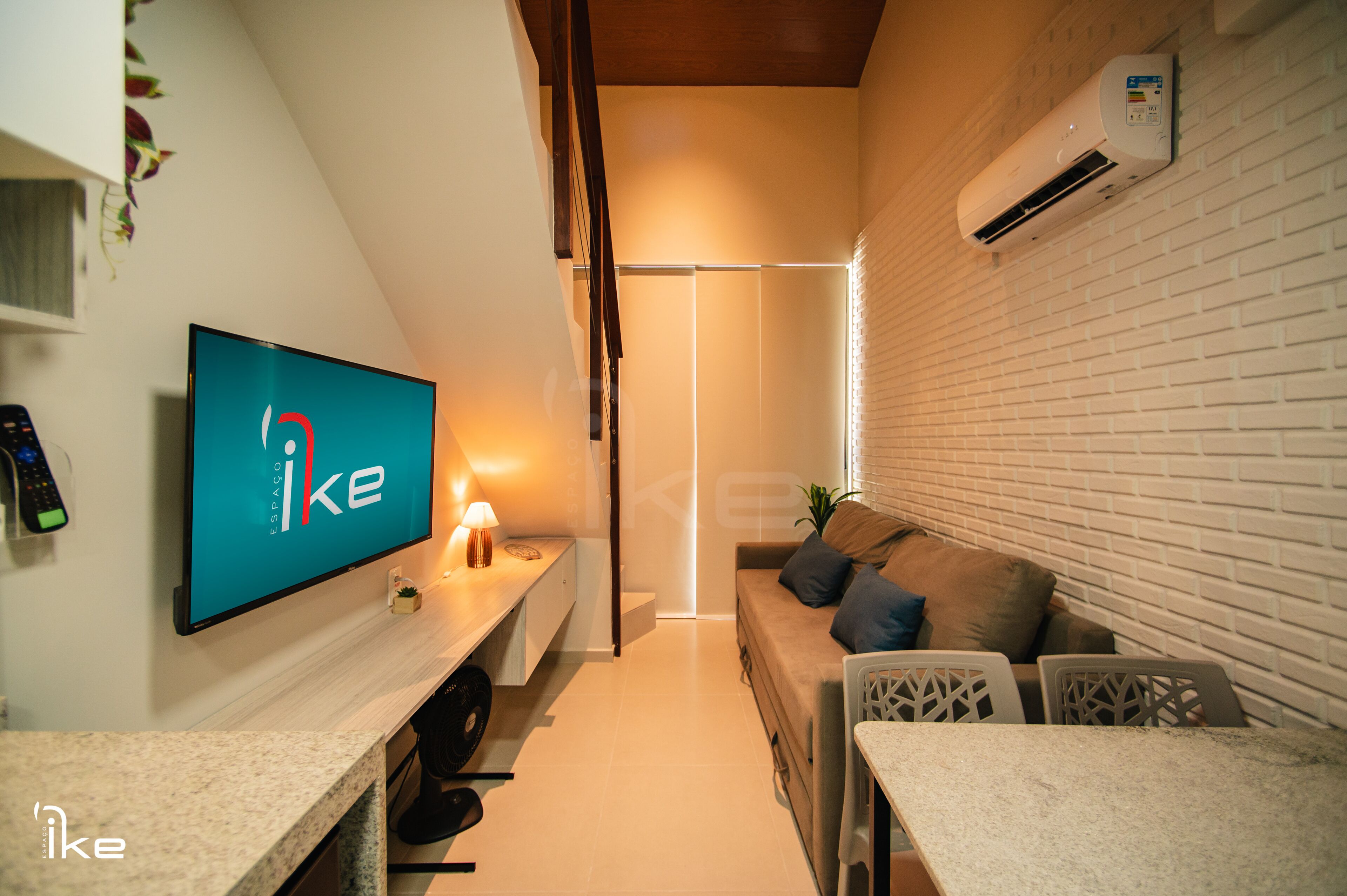 A modern living room with a flat-screen TV, a sofa with cushions, a coffee table, and a white brick wall.