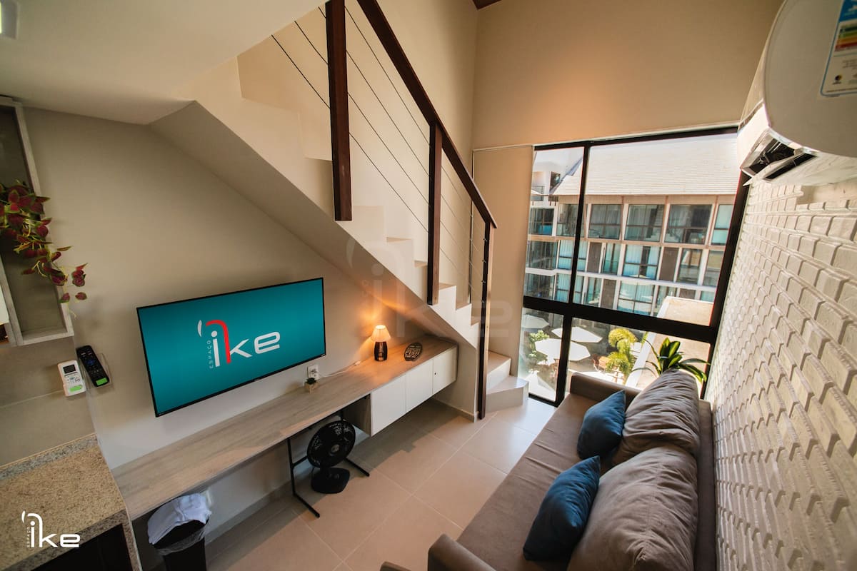 Una sala de estar moderna con un televisor de pantalla plana, una escalera y un amplio ventanal con vistas al exterior.