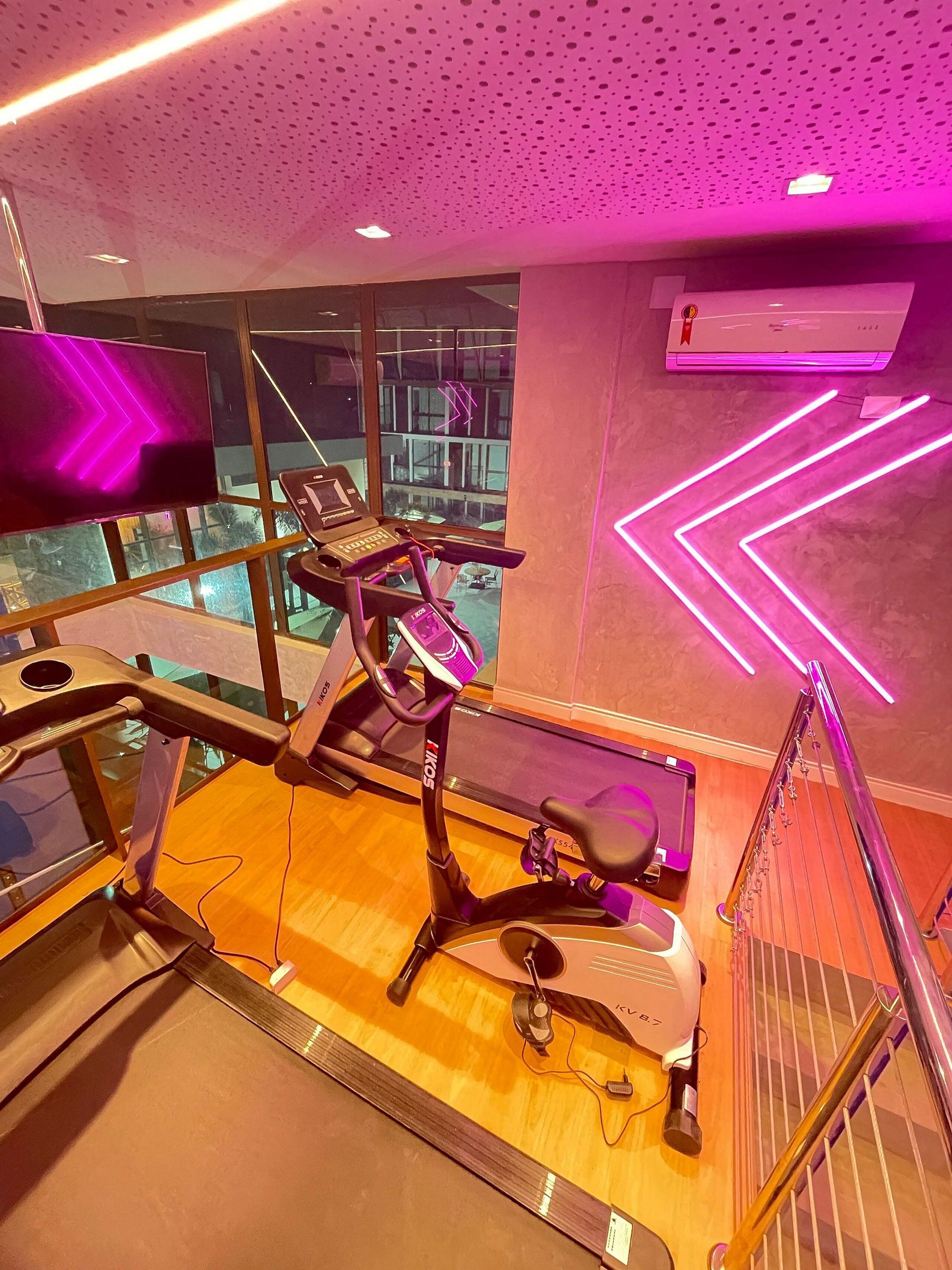 Une salle de sport équipée de matériel d’exercice, dotée d’une grande fenêtre et d’un éclairage néon décoratif sur le mur.