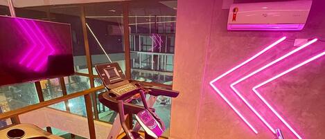 Une salle de sport équipée de matériel d’exercice, dotée d’une grande fenêtre et d’un éclairage néon décoratif sur le mur.
