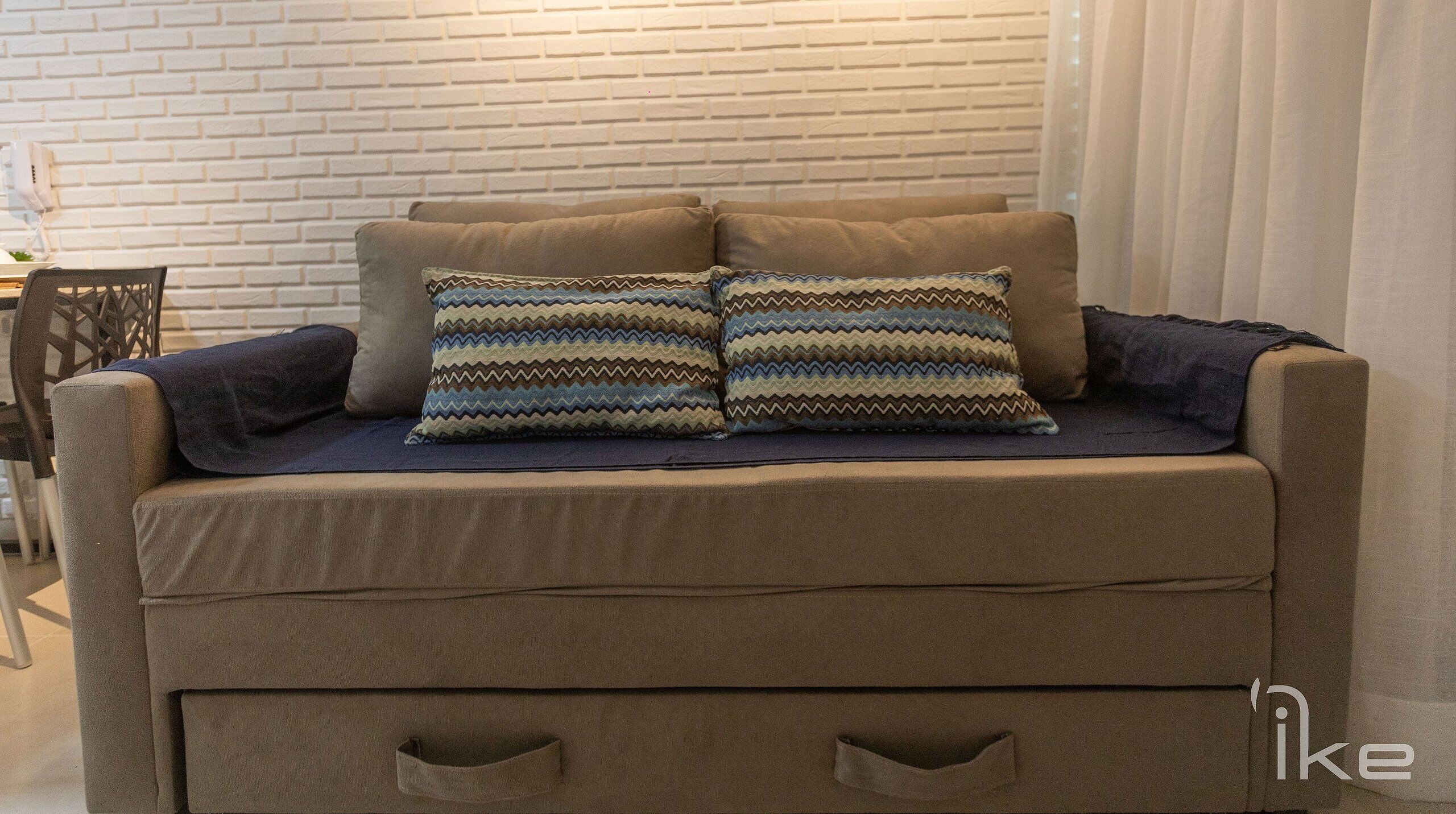 Un sofá marrón con dos almohadones estampados y una manta oscura.