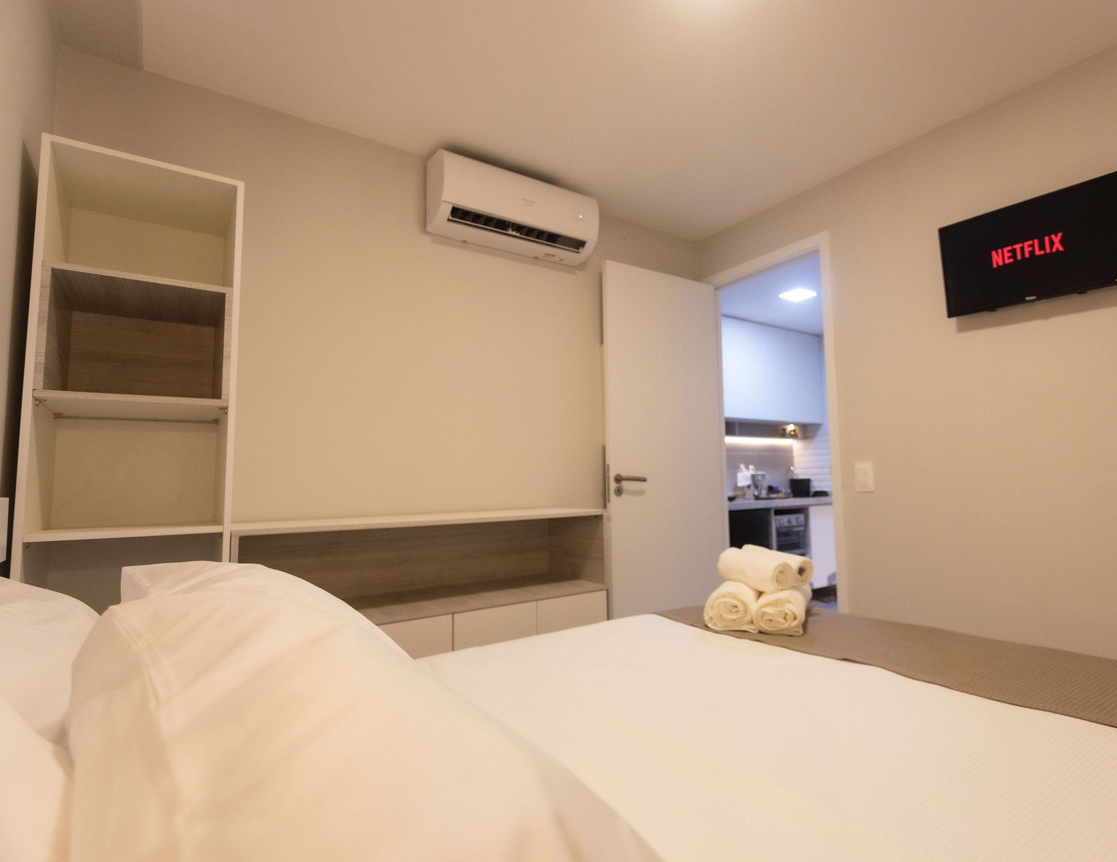 A hotel room with a bed, a TV mounted on the wall, an air conditioning unit, and a small table with towels.