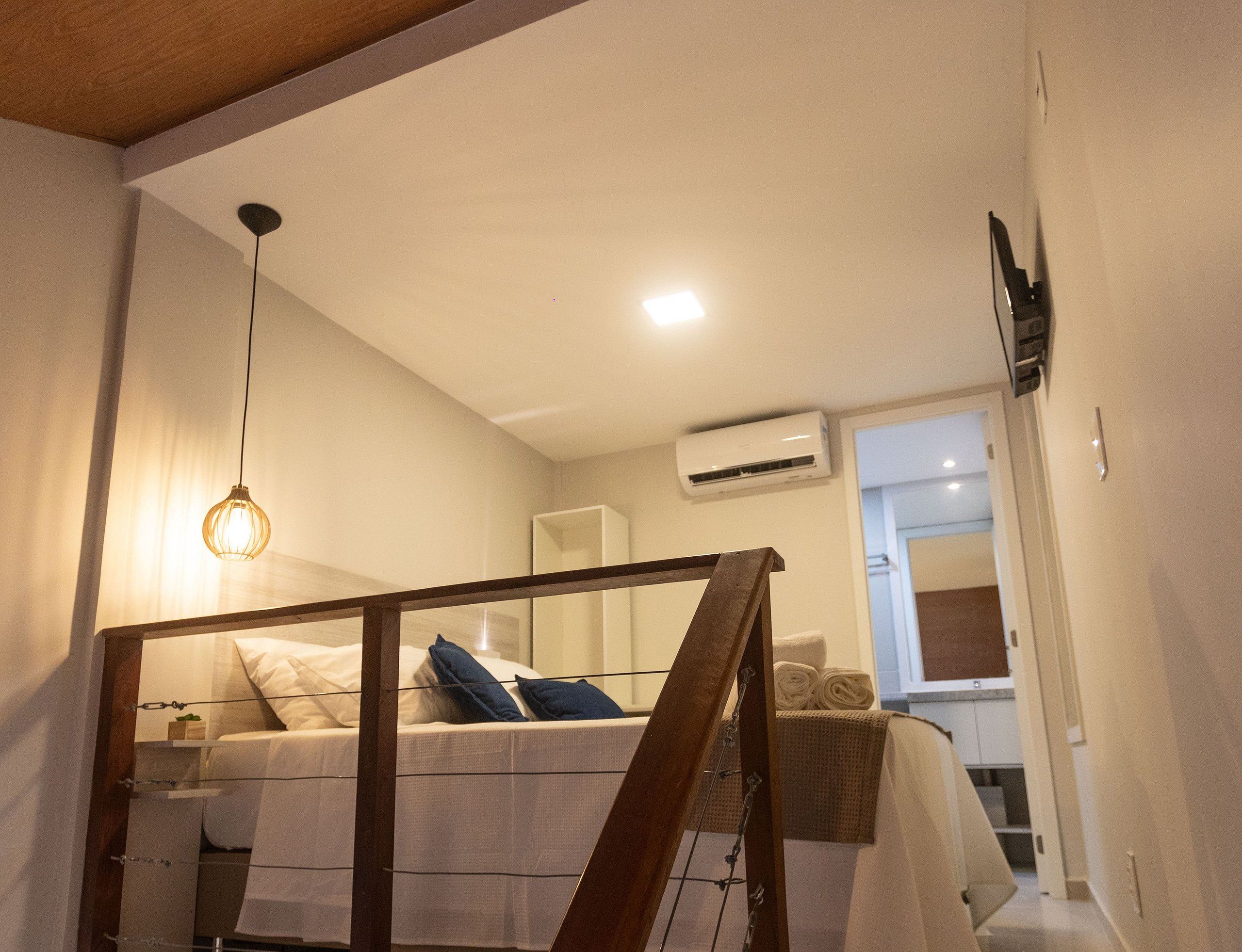 A bedroom with a bed, a hanging light fixture, an air conditioning unit, and a window.