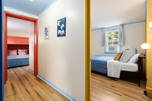 Habitación de hotel con piso de madera, una cama con cubrecama azul, una ventana con cortinas y una lámpara fijada a la pared.
