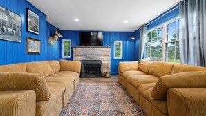 Una sala de estar con paredes azules, dos sofás color beige, un tapete estampado, una chimenea de piedra y cuadros enmarcados en la pared.