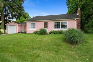 Una casa de un solo piso de color rosa, con garaje, un porche delantero y un césped bien cuidado.