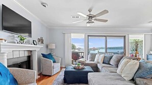 Una sala de estar con chimenea, ventilador de techo y ventanas amplias con vistas.