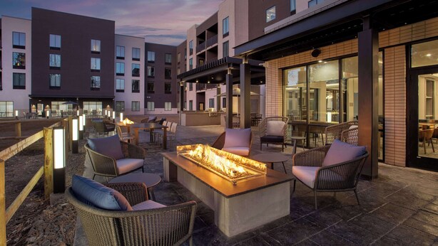 Eine Außenpatio-Terrasse mit Sitzgelegenheiten und einem Feuerbereich, umgeben von modernen Gebäuden.