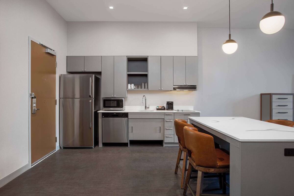 Una cocina moderna con electrodomésticos de acero inoxidable, una isla central y taburetes de bar.