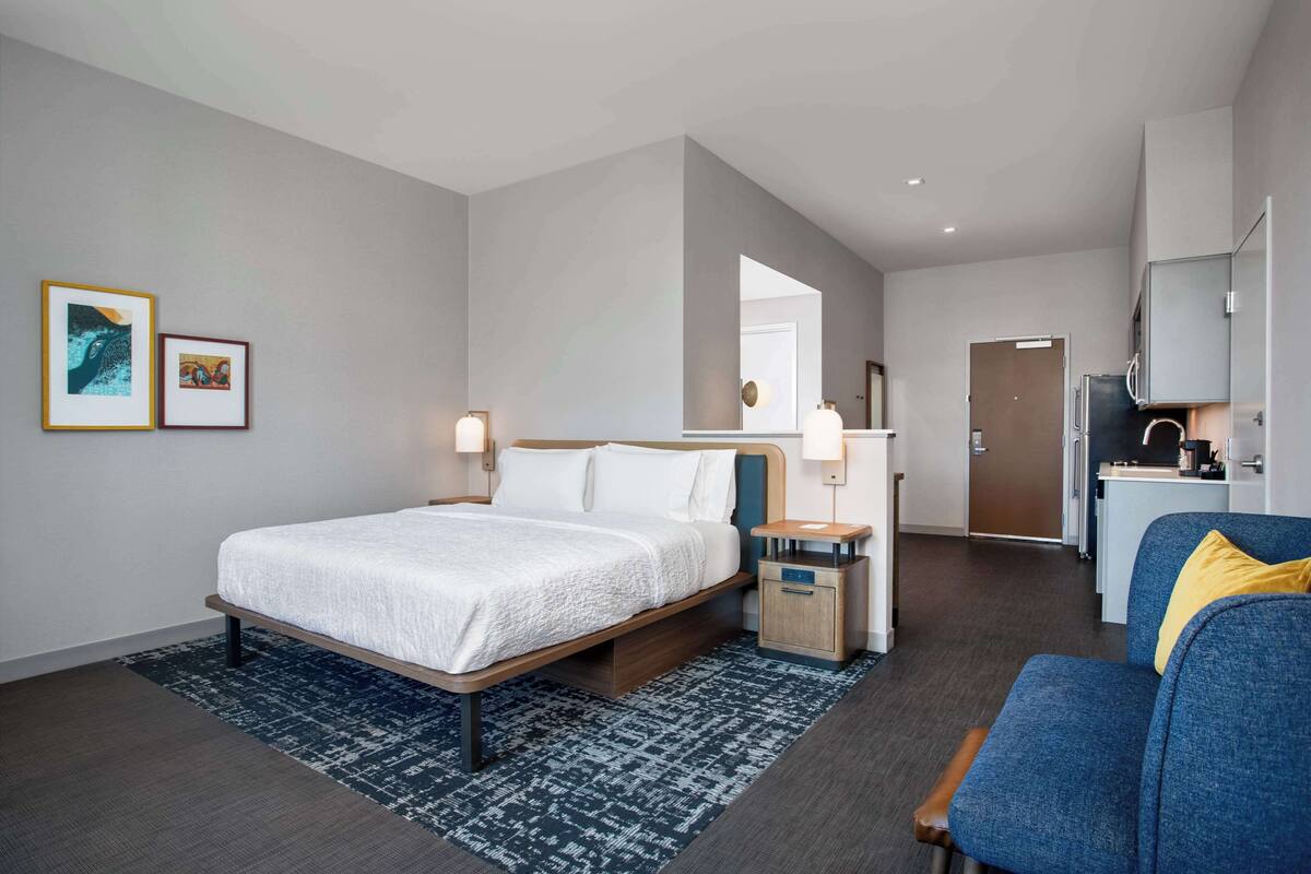 Una habitación de hotel moderna con una cama grande, un escritorio pequeño, una silla y un rincón americano.