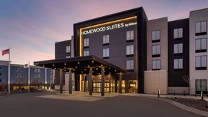 A modern hotel with a sign reading "HOMEWOOD SUITES by Hilton" and a covered entrance.