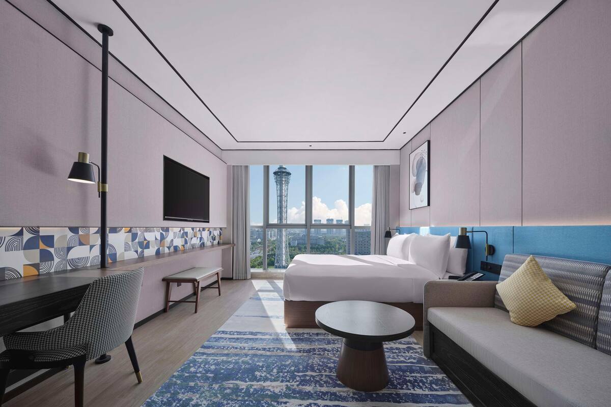 A modern hotel room with a large bed, a sofa, a dining table, and a TV mounted on the wall.