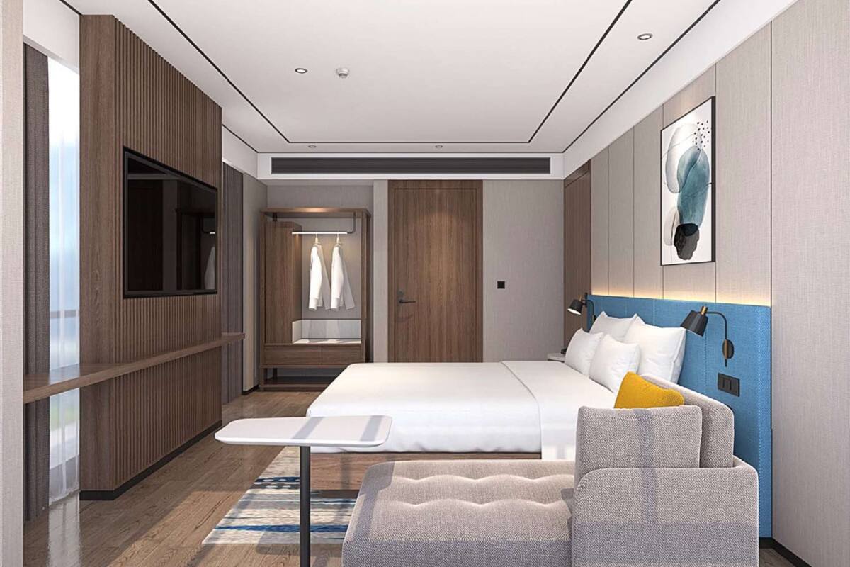 A modern hotel room with a large bed, a seating area, a flat-screen TV, and a door leading to a bathroom.