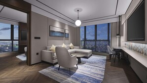 Ein modernes Wohnzimmer mit einer Couch, Sesseln, einem Couchtisch und einem Essbereich mit Tisch und Stühlen. Große Fenster bieten Blick auf die Stadt.
