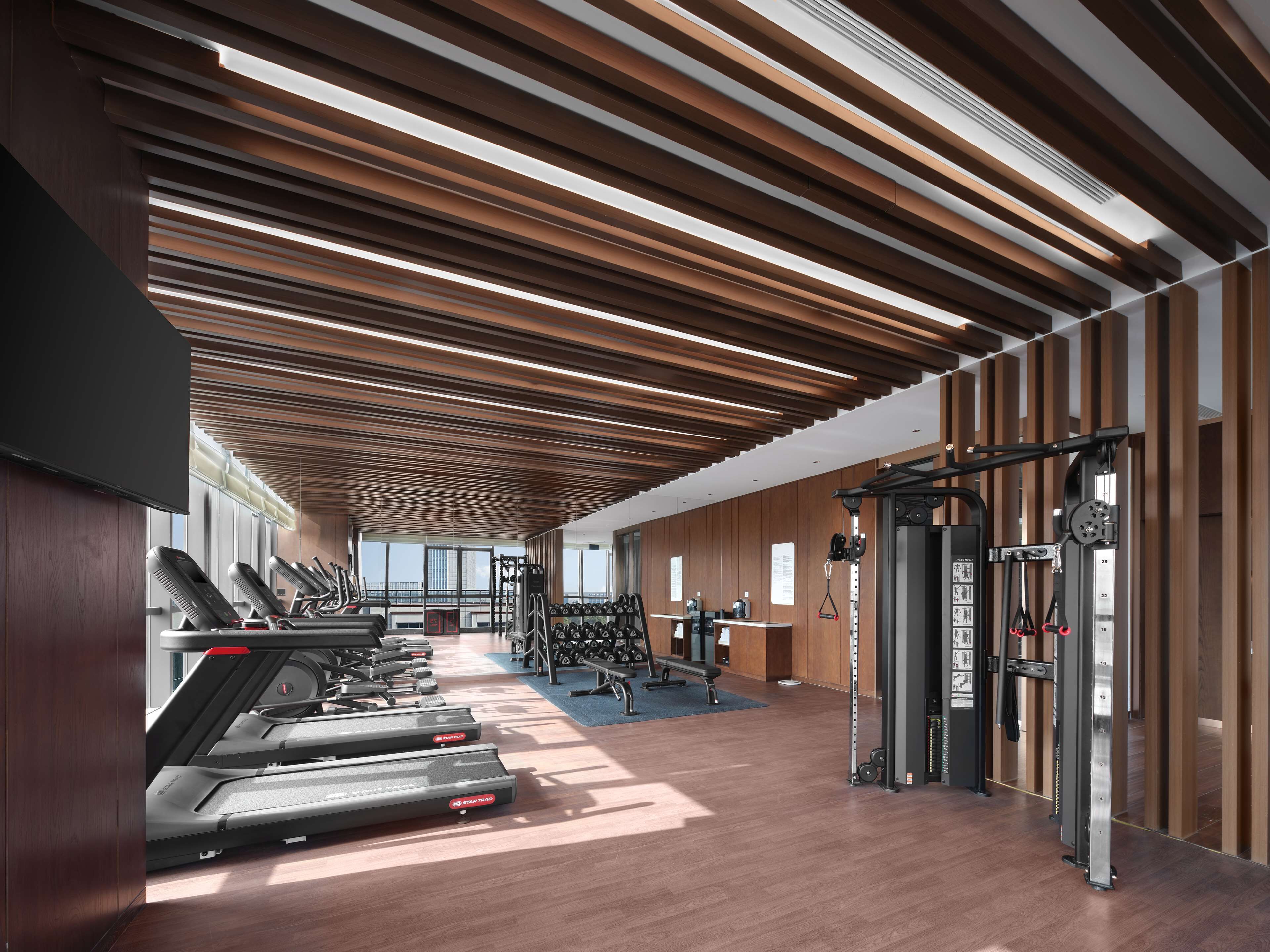 Une salle de sport moderne équipée de tapis de course, d’appareils de musculation et dotée d’un plafond en bois.