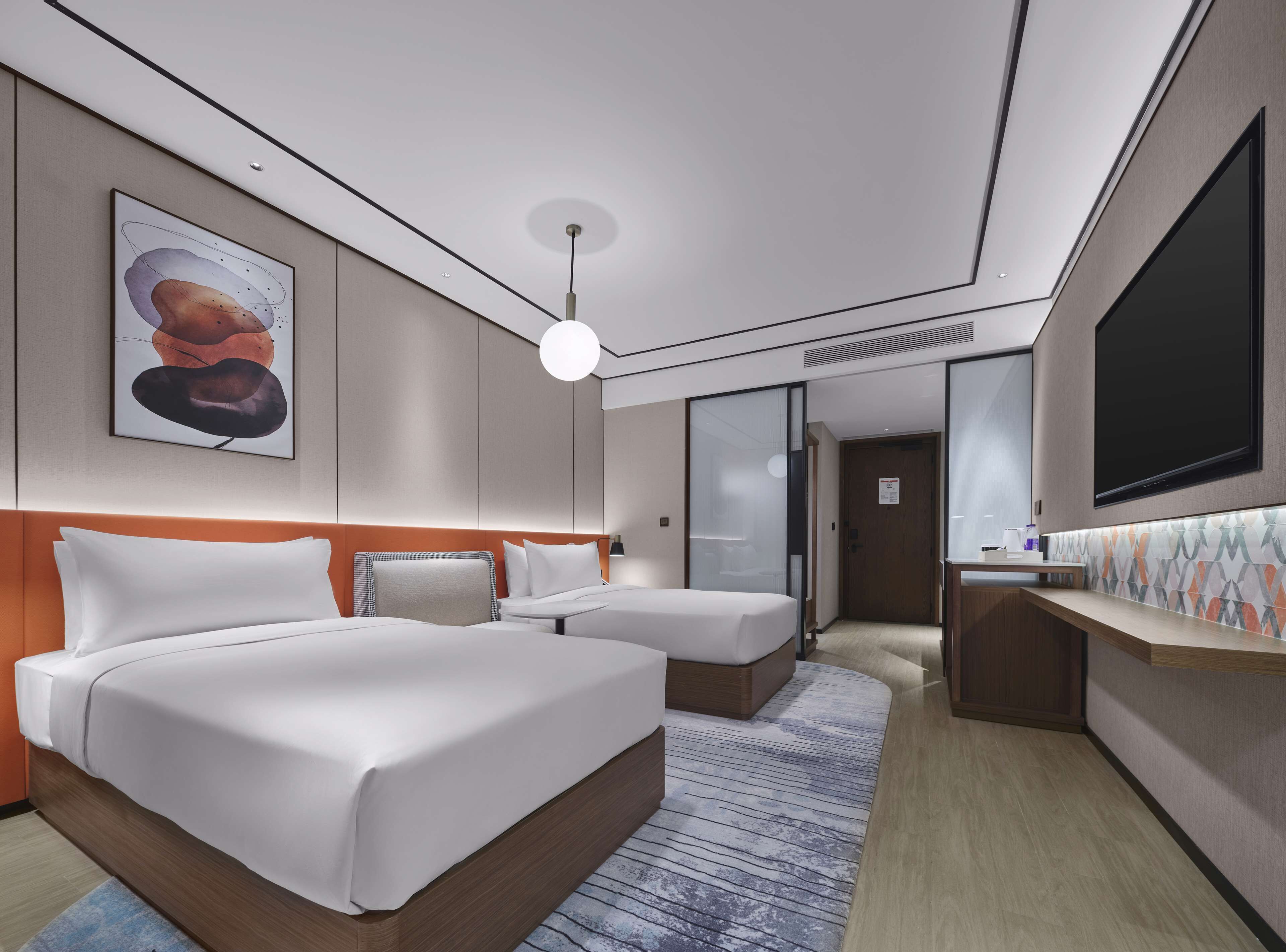 A modern hotel room with two beds, a large artwork on the wall, a flat-screen TV, and a small desk area.
