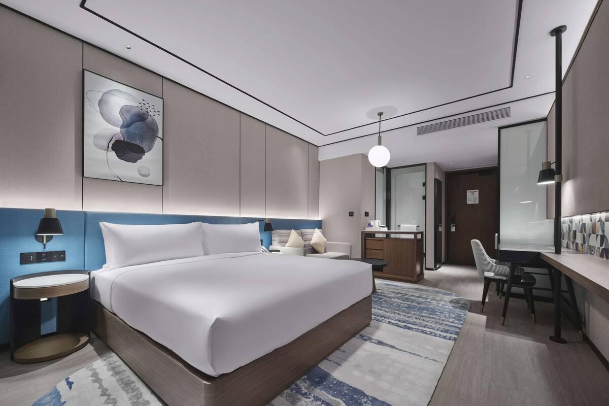 A modern hotel room with a large bed, bedside tables, a desk, and a mirror.