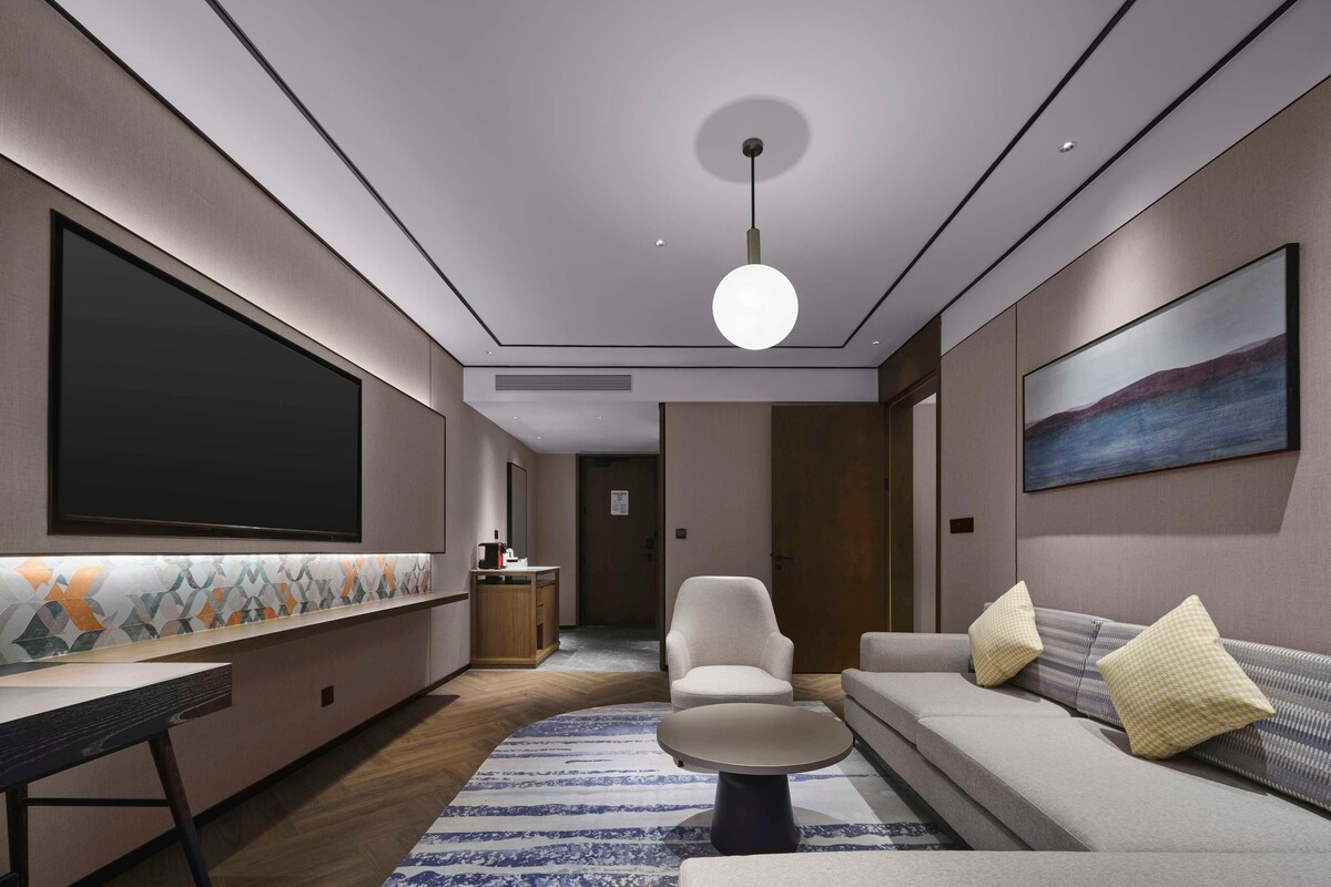 A modern living room with a large flat-screen TV, a sofa, a coffee table, and a chair.