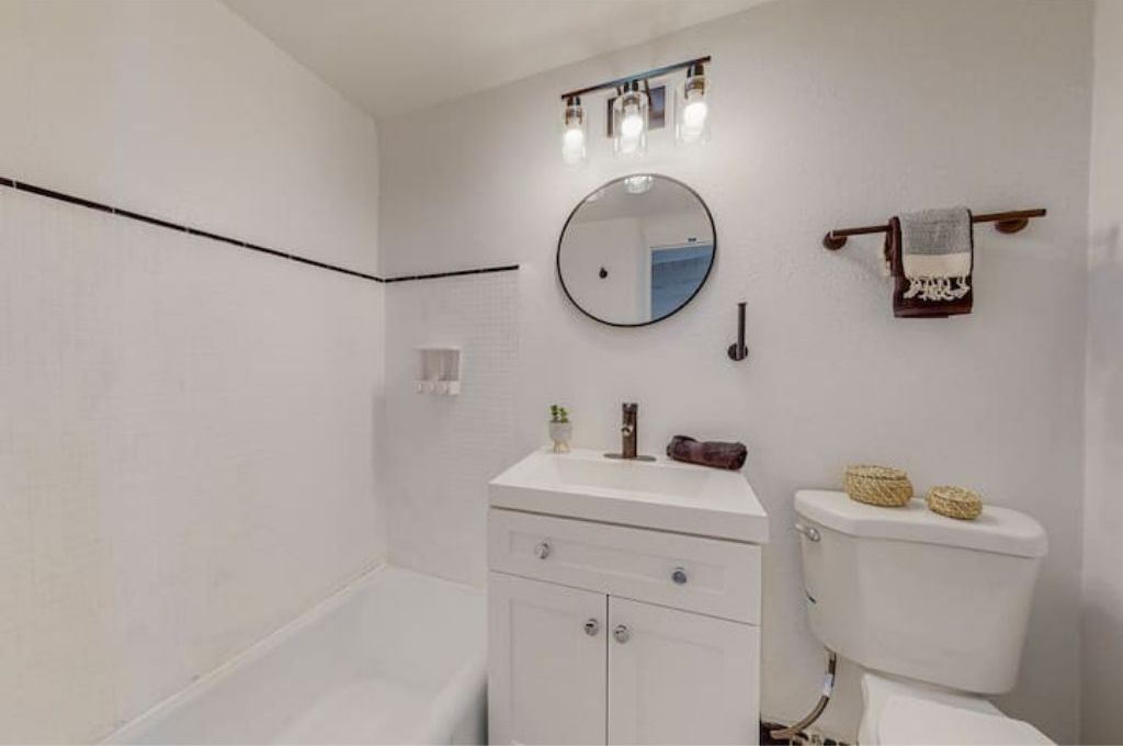 A bathroom with a white vanity, a round mirror, a towel rack, and a toilet.