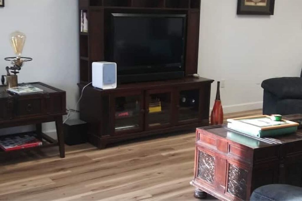 Una sala de estar con un mueble de centro de entretenimiento de madera oscura, un televisor de pantalla plana, un altavoz blanco pequeño y una lámpara decorativa.