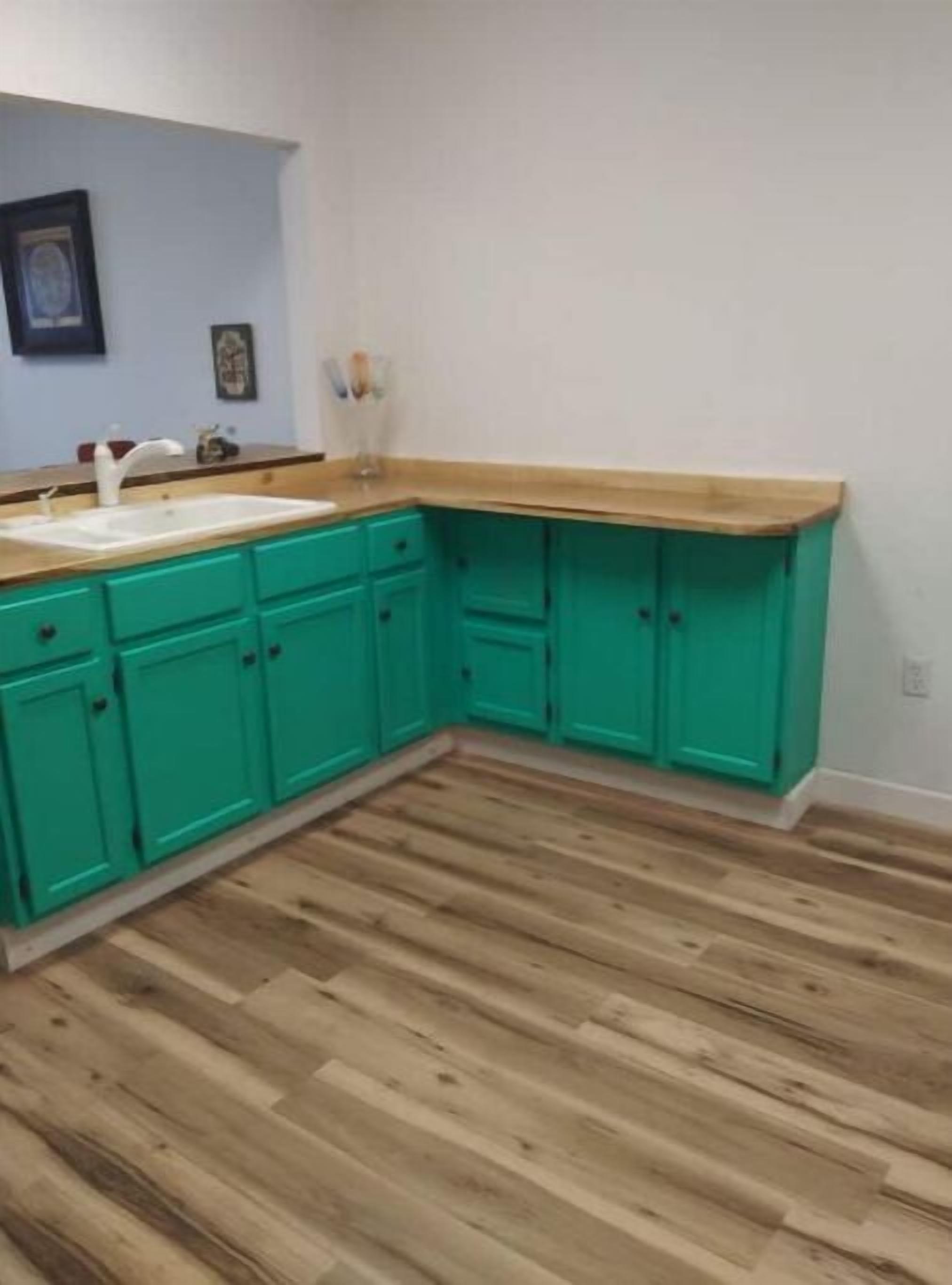 A kitchen with teal cabinets, a wooden countertop, and a wooden floor.