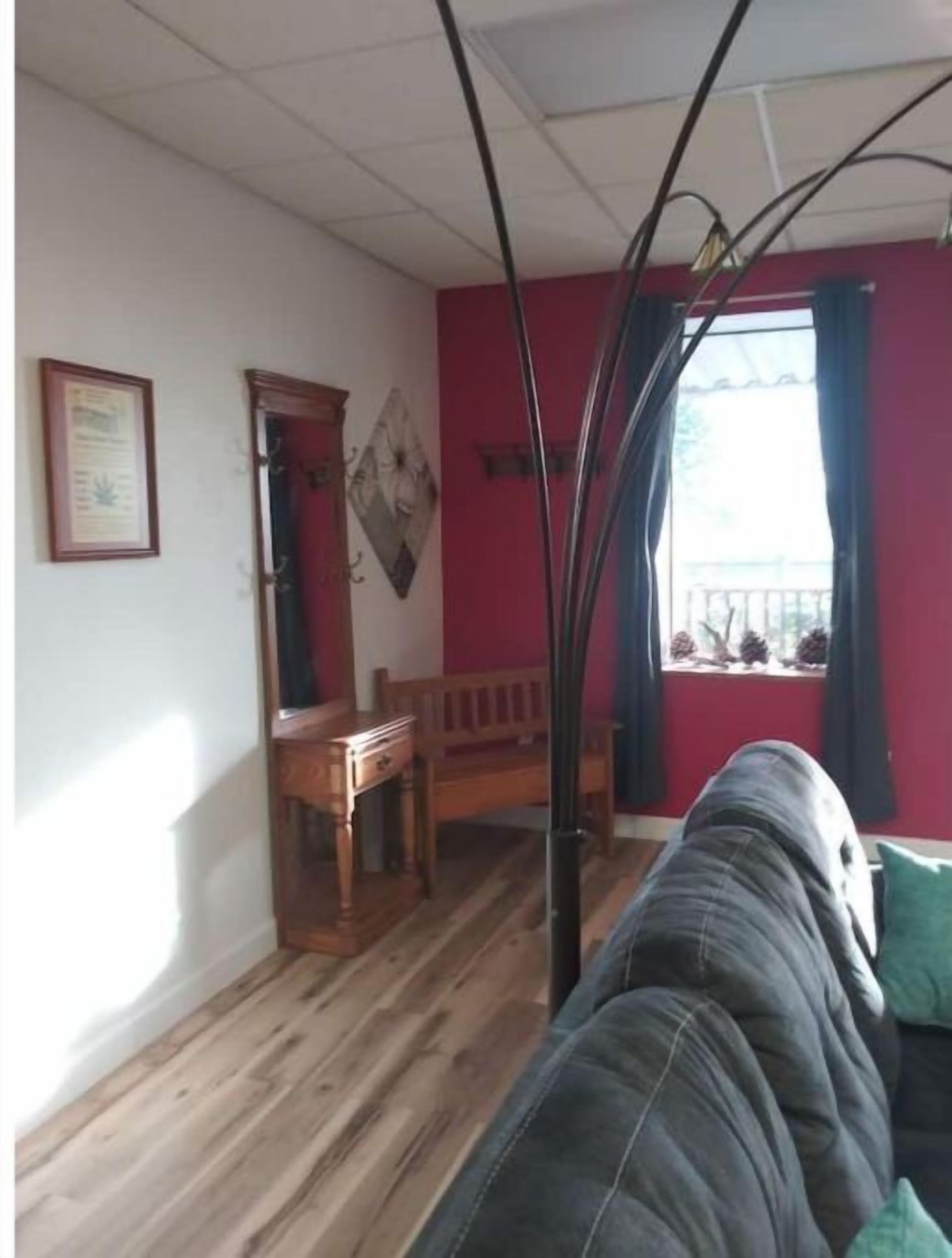 A room with a wooden floor, a red wall, a window with curtains, a wooden bench, and a framed certificate on the wall.
