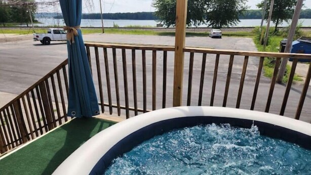 Ein Whirlpool mit Wasser, eine Holzterrasse und Blick auf eine Straße und Bäume.